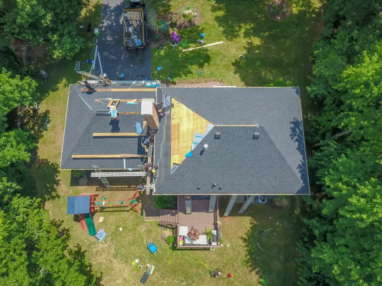 Aerial view of residential home with gray roof and attached garage surrounded by trees