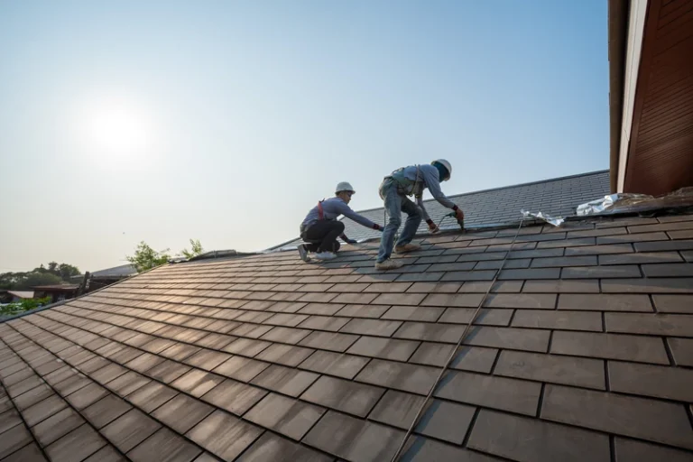 Two workers installing or repairing roof shingles on residential home during daytime
