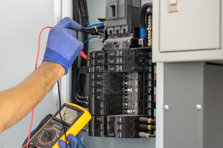 Technician in blue gloves repairing electrical control panel with tools