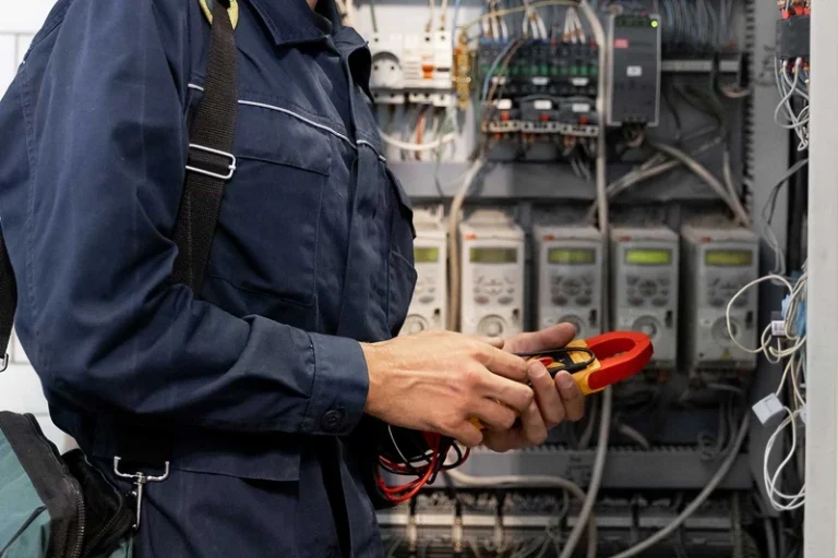 Technician in blue uniform using multimeter to test electrical panel connections