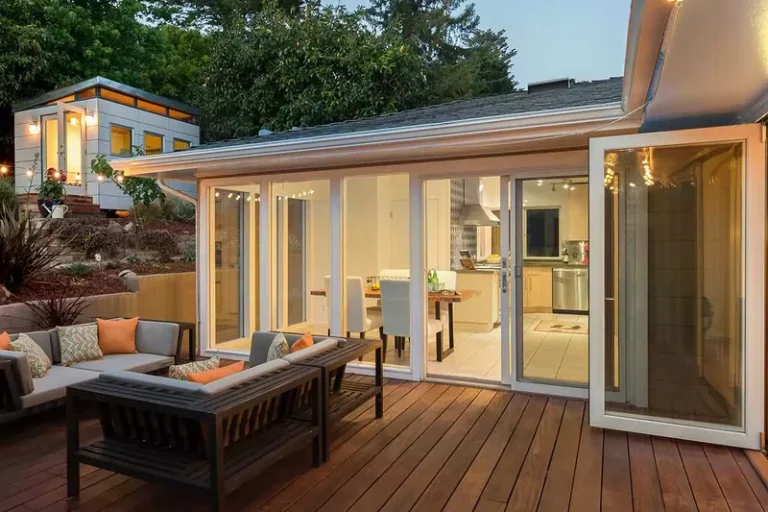Residential deck with wooden flooring and attached yellow home addition featuring large windows and doors