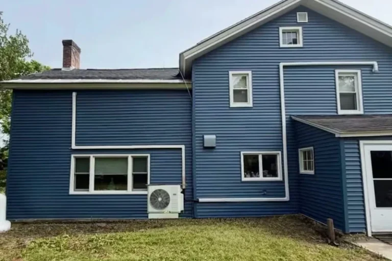 Blue residential house exterior with white trim and air conditioning unit installed on side wall